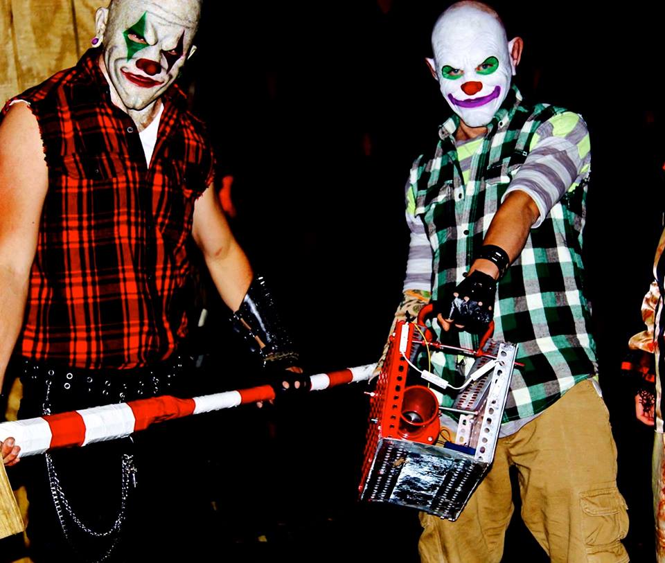 Two people in clown masks holding a red and white prop weapon
