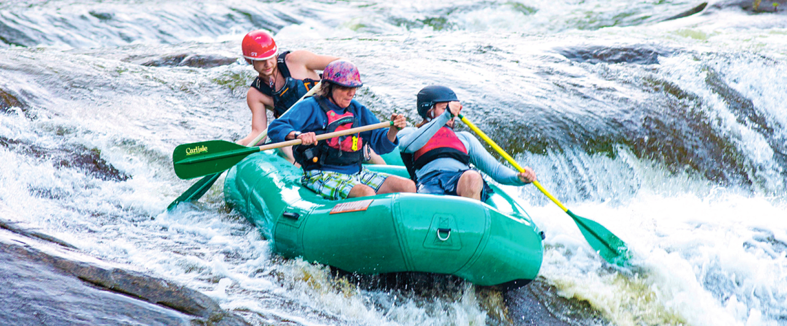 Three people whitewater rafting on a river with rapids