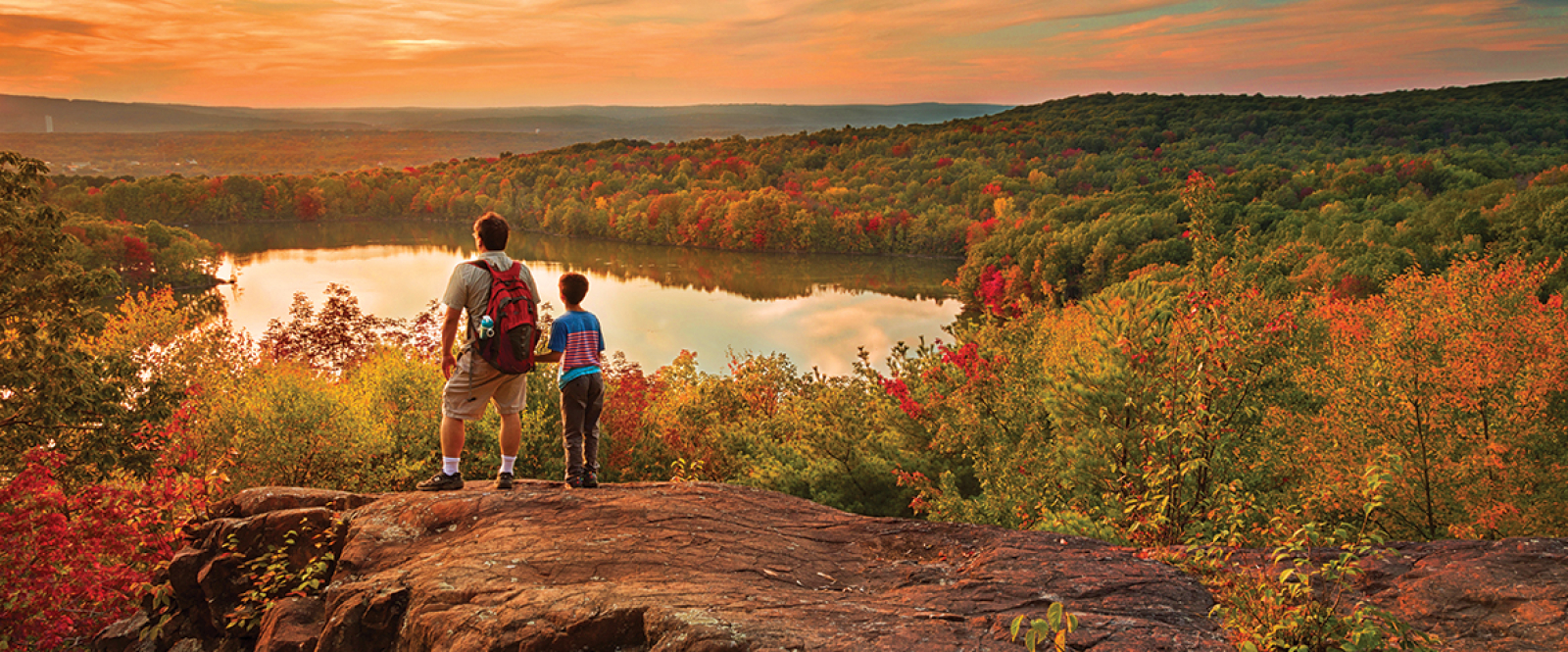 Two hikers overlook Crescent Lake surrounded by autumn foliage at sunset