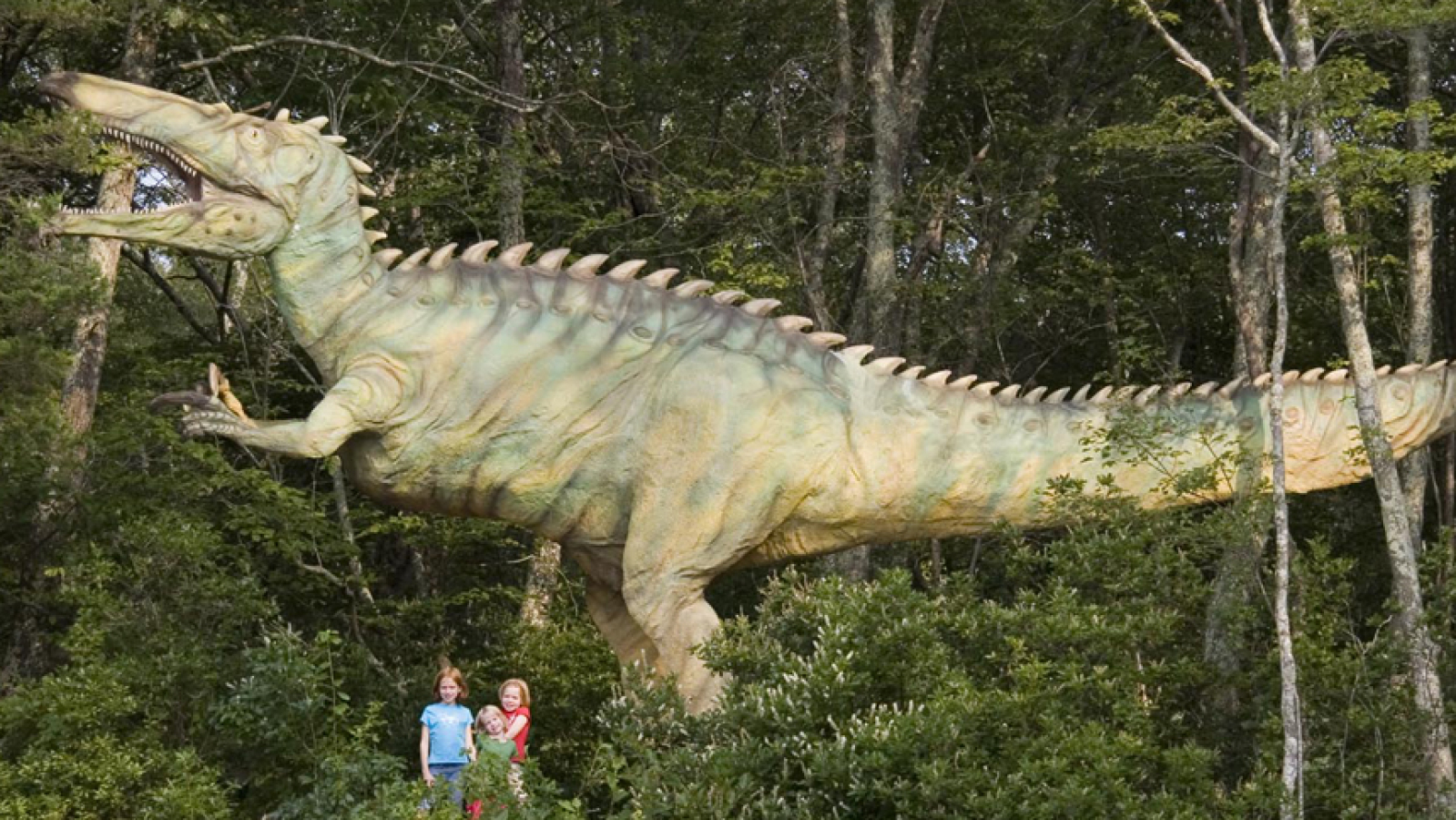 Children standing next to a dinosaur statue