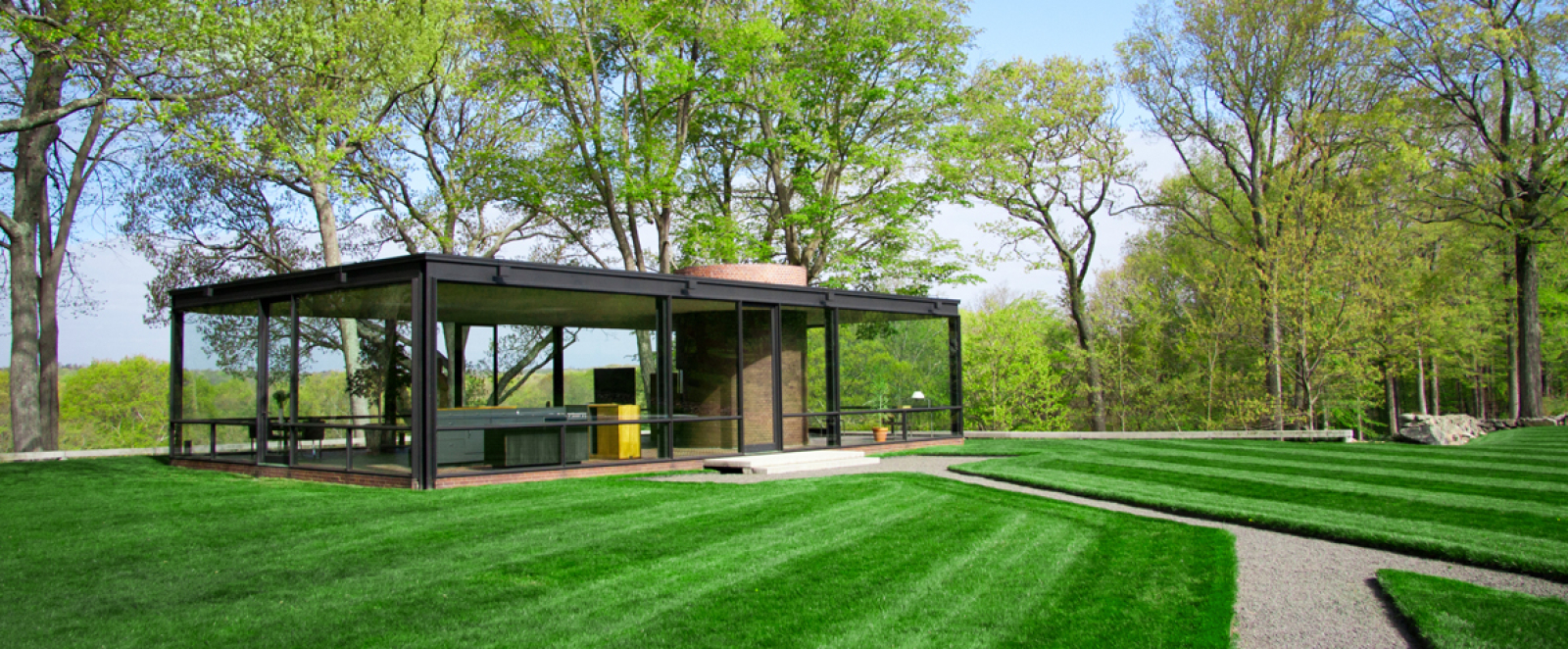 Historic Glass House with glass walls surrounded by manicured lawn and trees