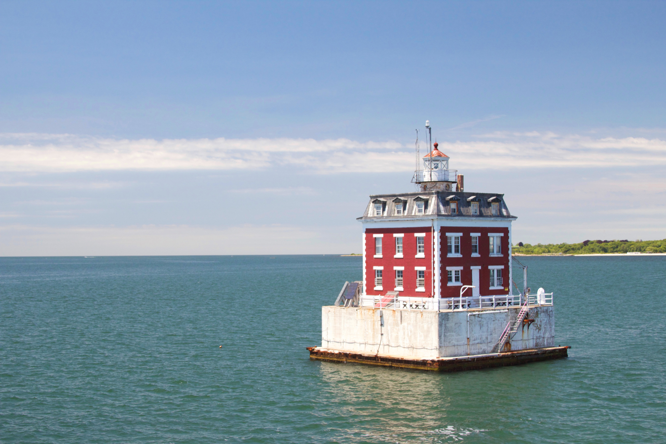 Historic red and white lighthouse on concrete base in ocean near shoreline