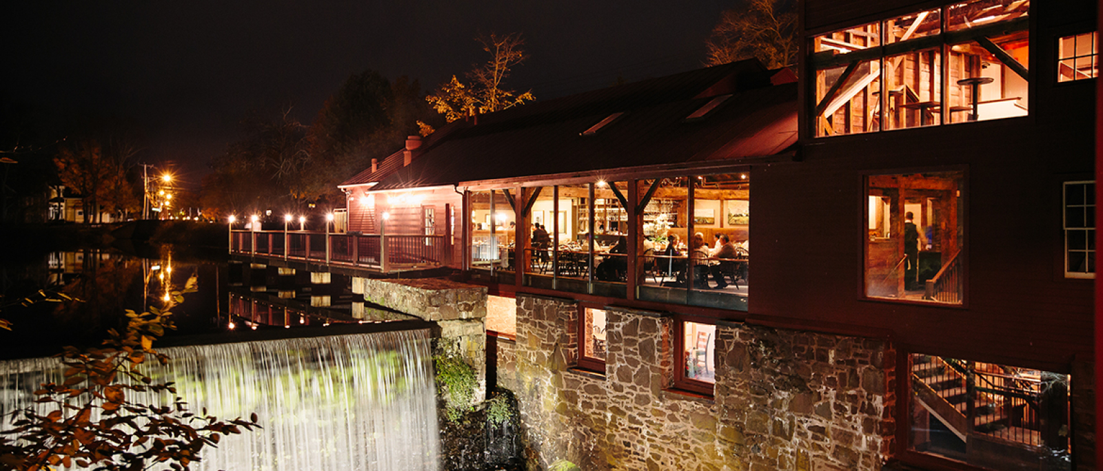Historic mill building restaurant illuminated at night by waterfall