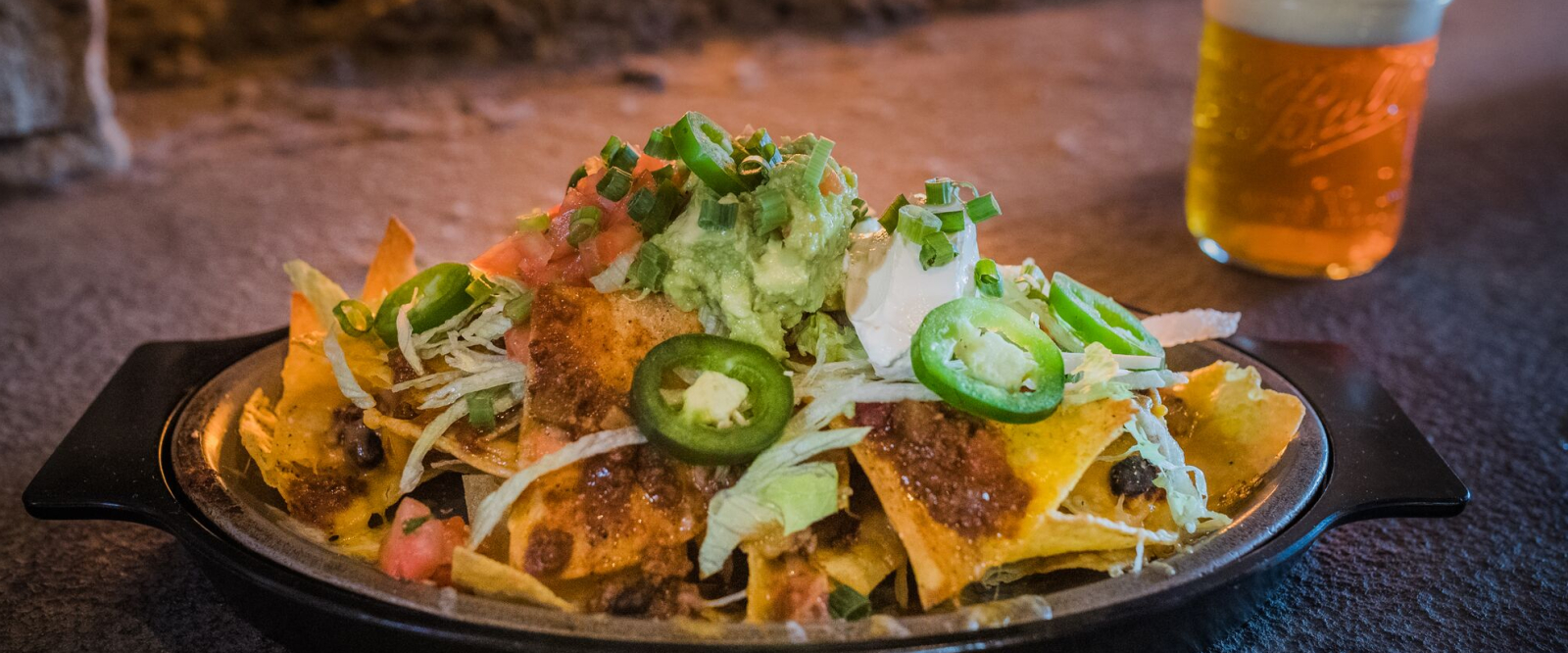 Plate of nachos topped with jalape√±os, guacamole, sour cream, and green onions