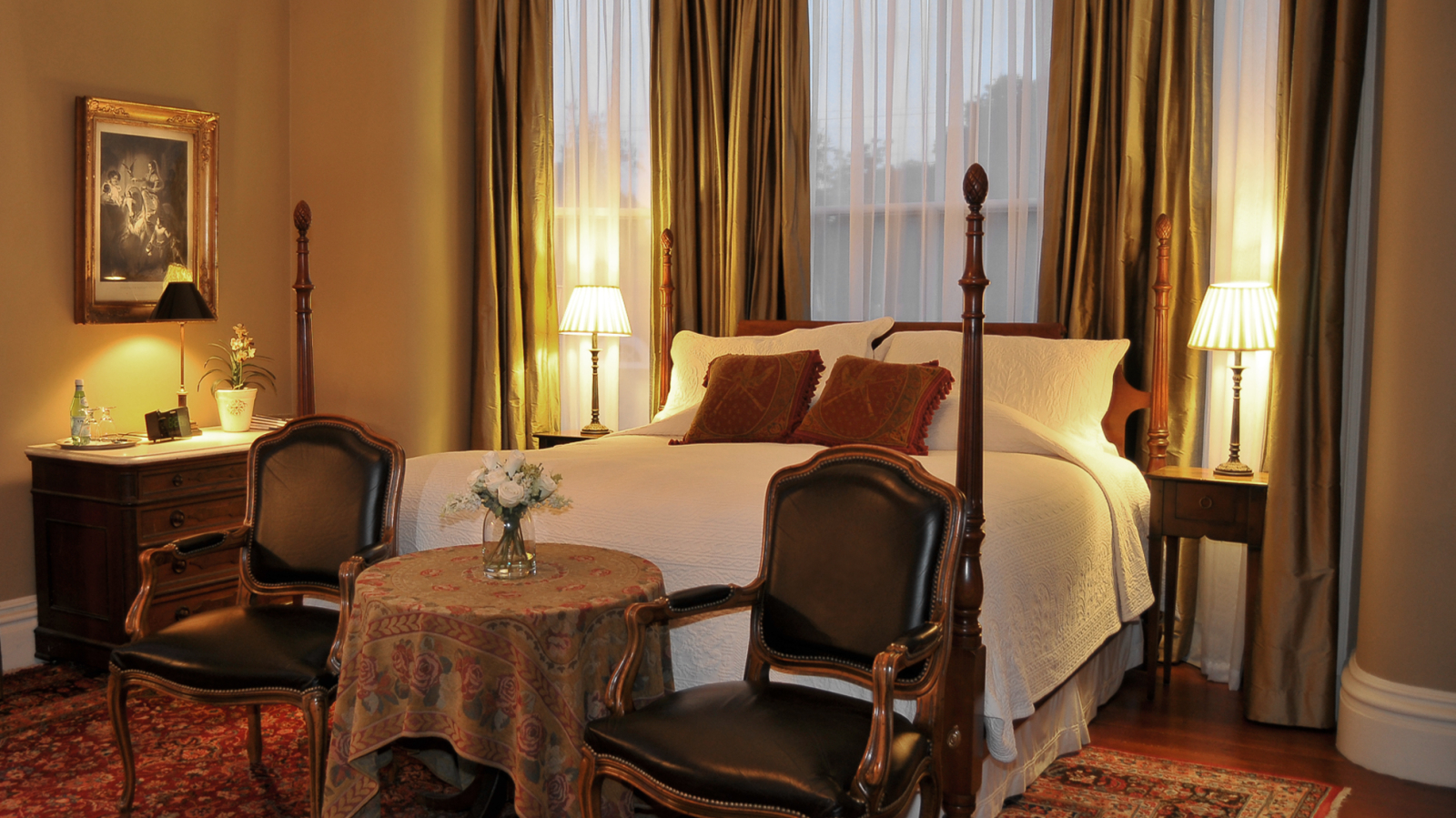 Elegant bedroom with four-poster bed, vintage chairs, and warm lighting