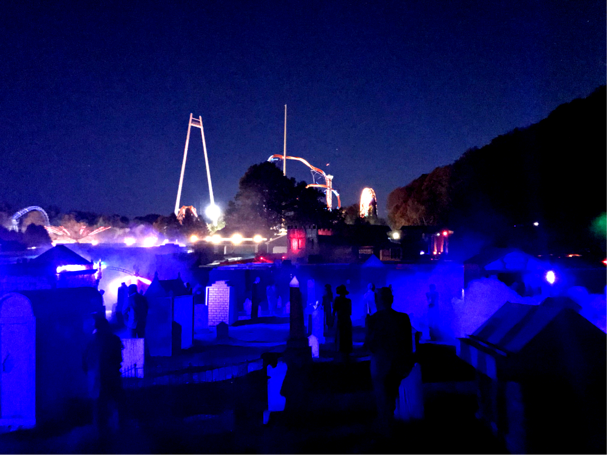 Dark haunted graveyard with glowing blue fog and amusement park rides behind