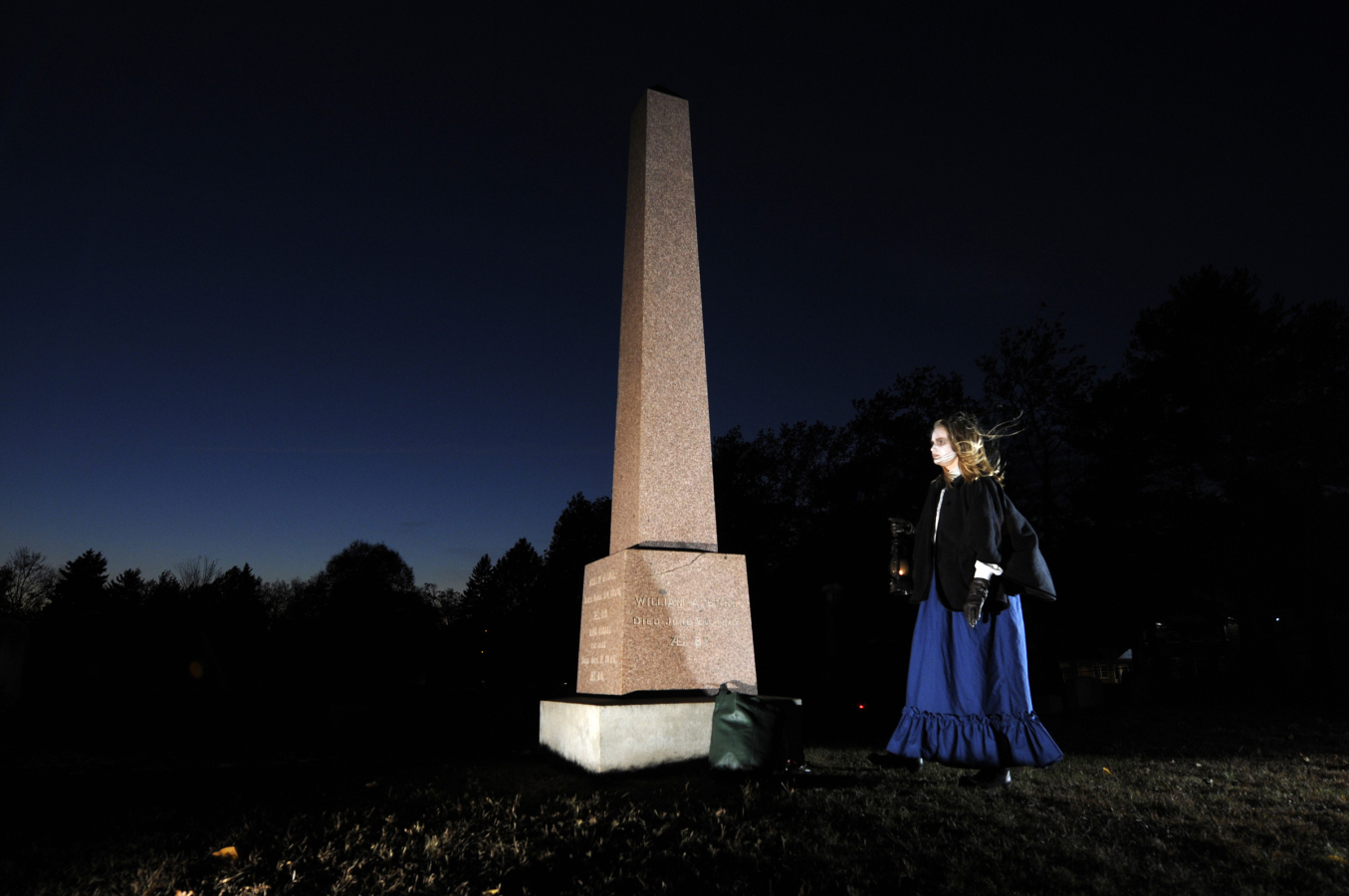Person holding lantern near tall grave monument at night