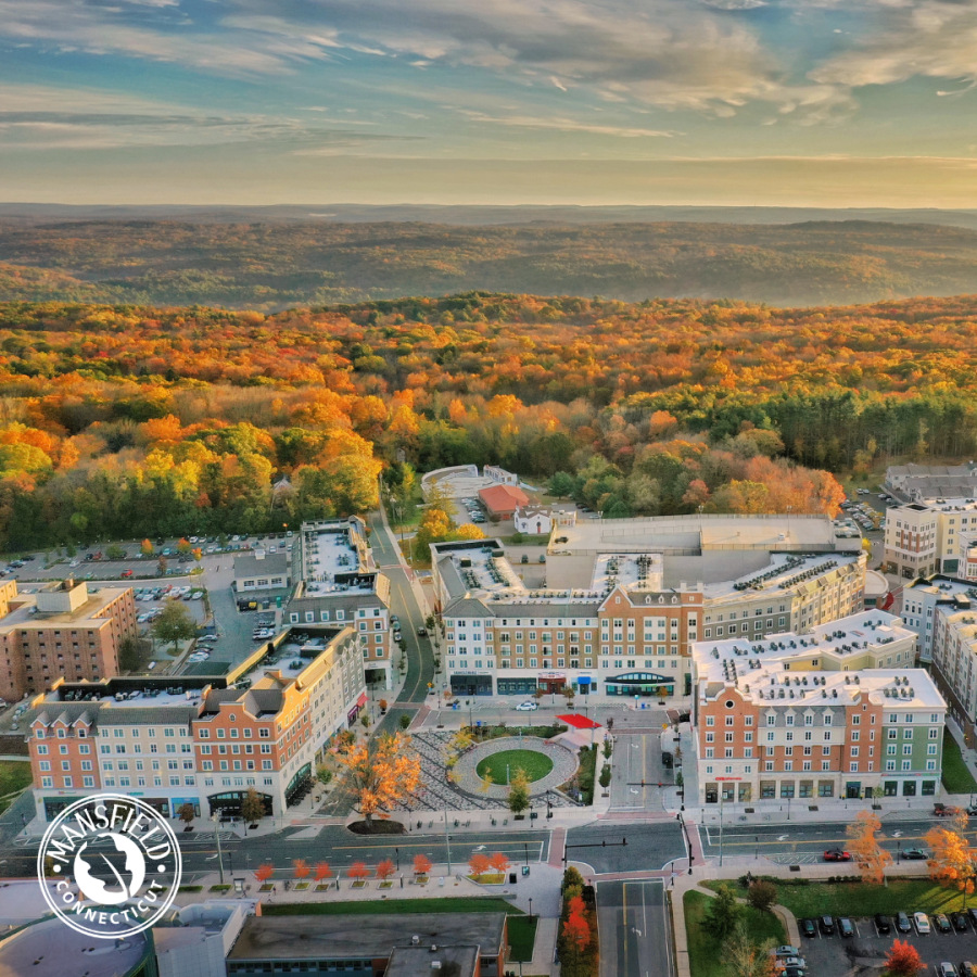 An aerial view of a downtown neighborhood with rolling hills emblazoned in fall colors in the distance