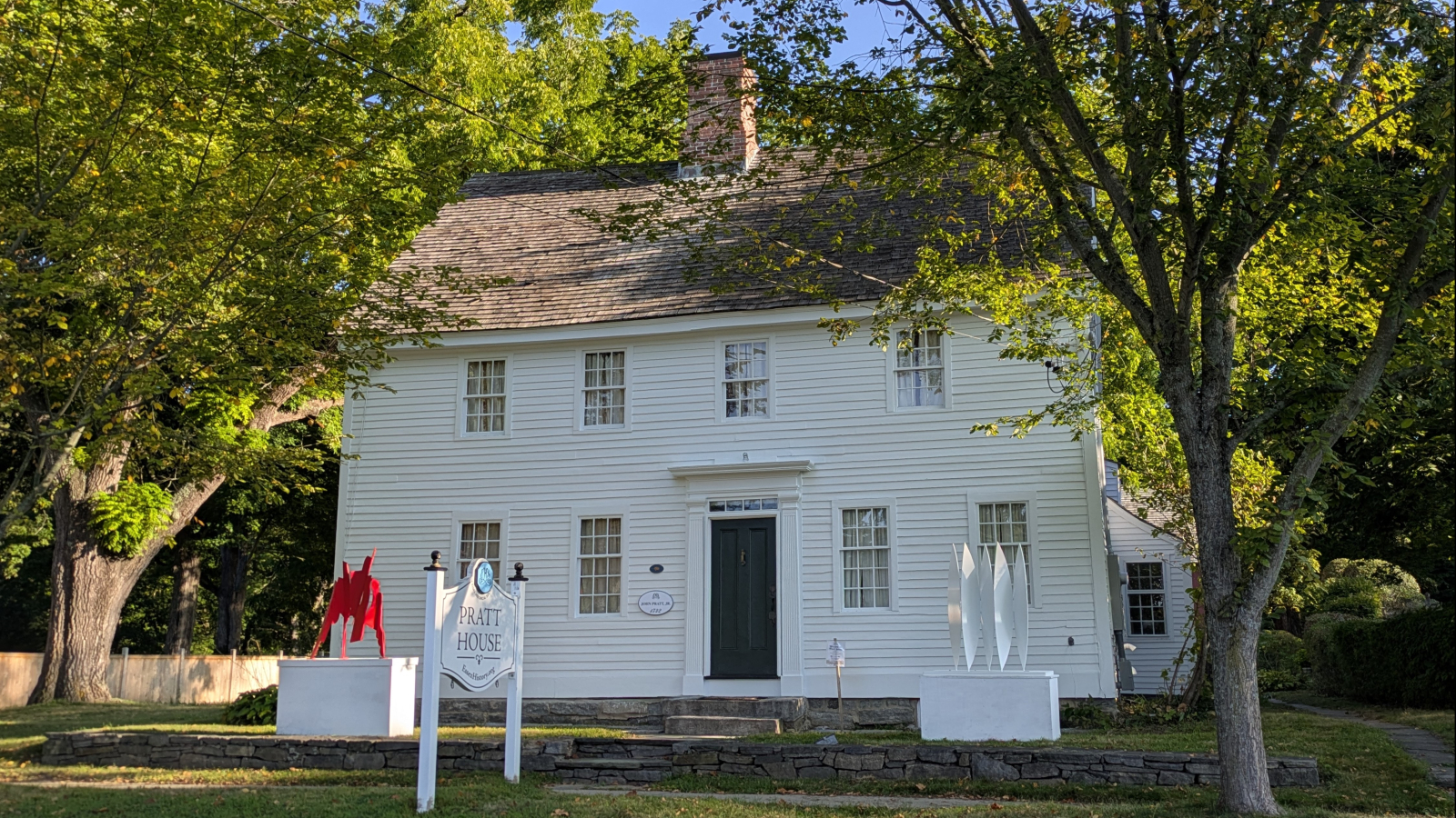 Pratt House in summer with leafy trees and modern art on display