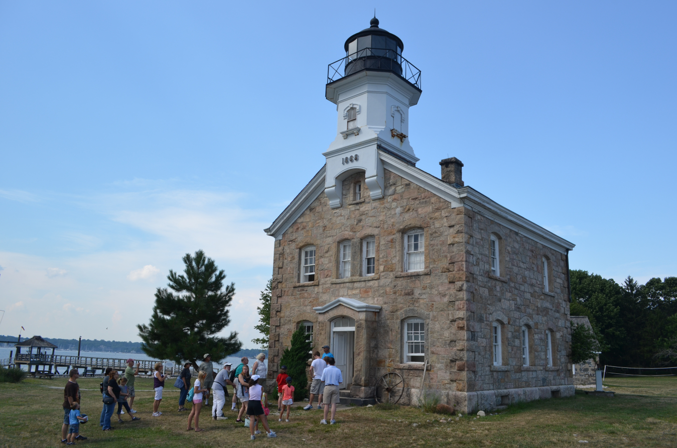 Stone lighthouse with people gathered outside near waterfront