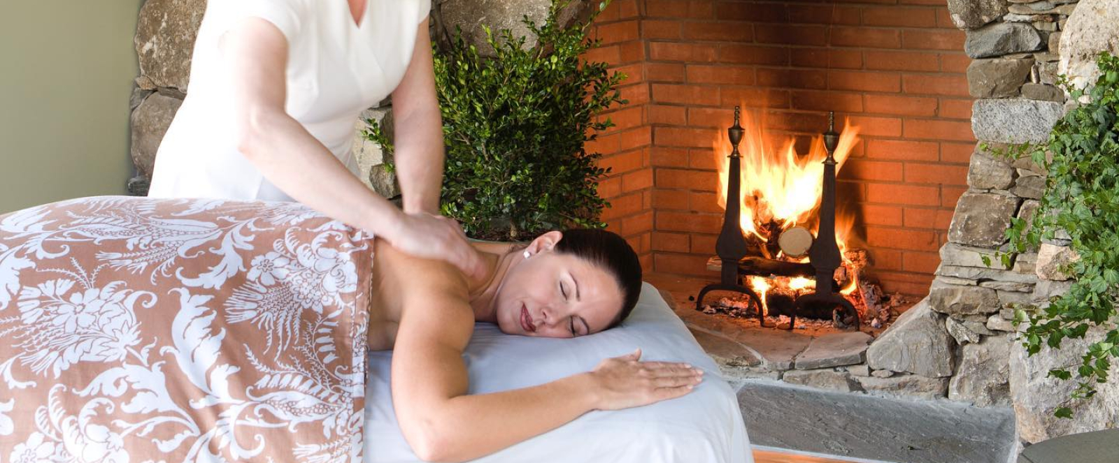 Woman receiving back massage near stone fireplace with lit candles