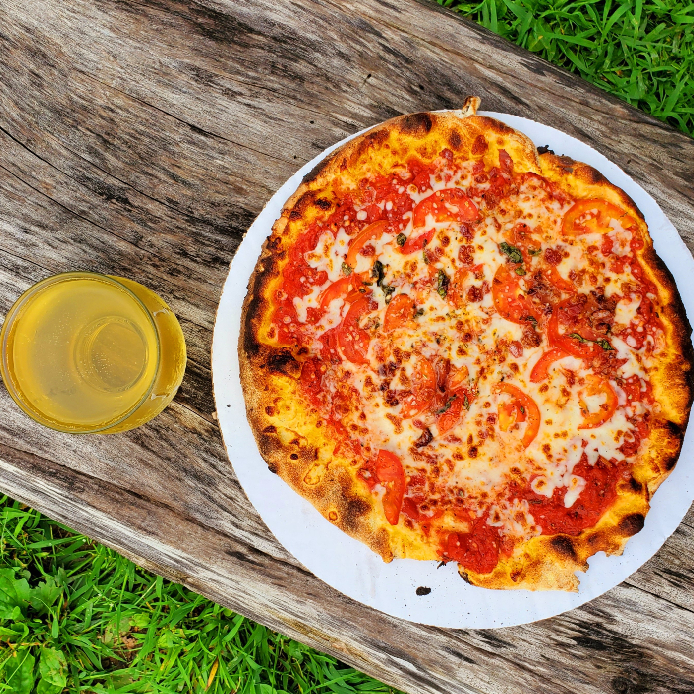 Tomato and cheese pizza on paper plate with drink on wooden table