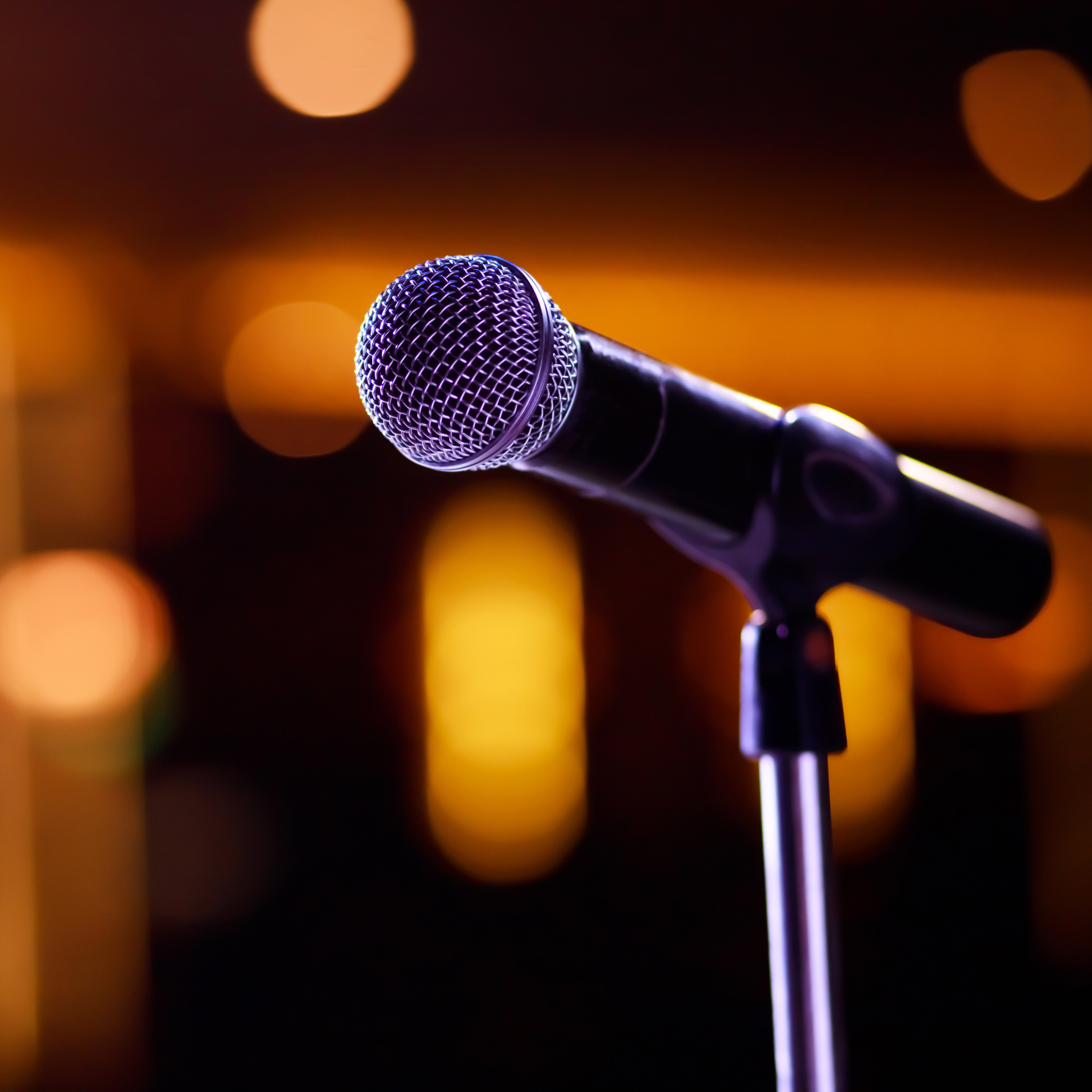 Close-up of a microphone on a stand with warm, blurred stage lights in the background.