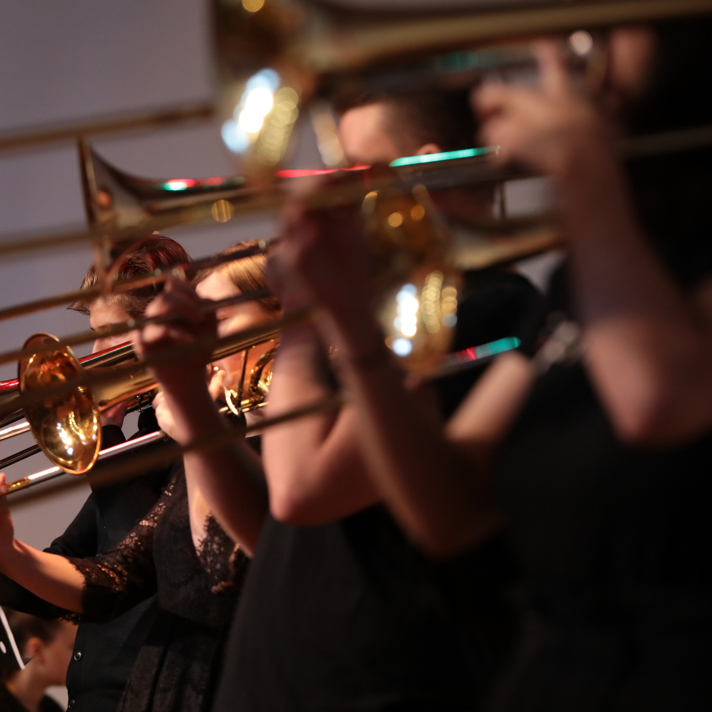 Brass musicians performing with trombones and trumpets on stage, viewed from the side.