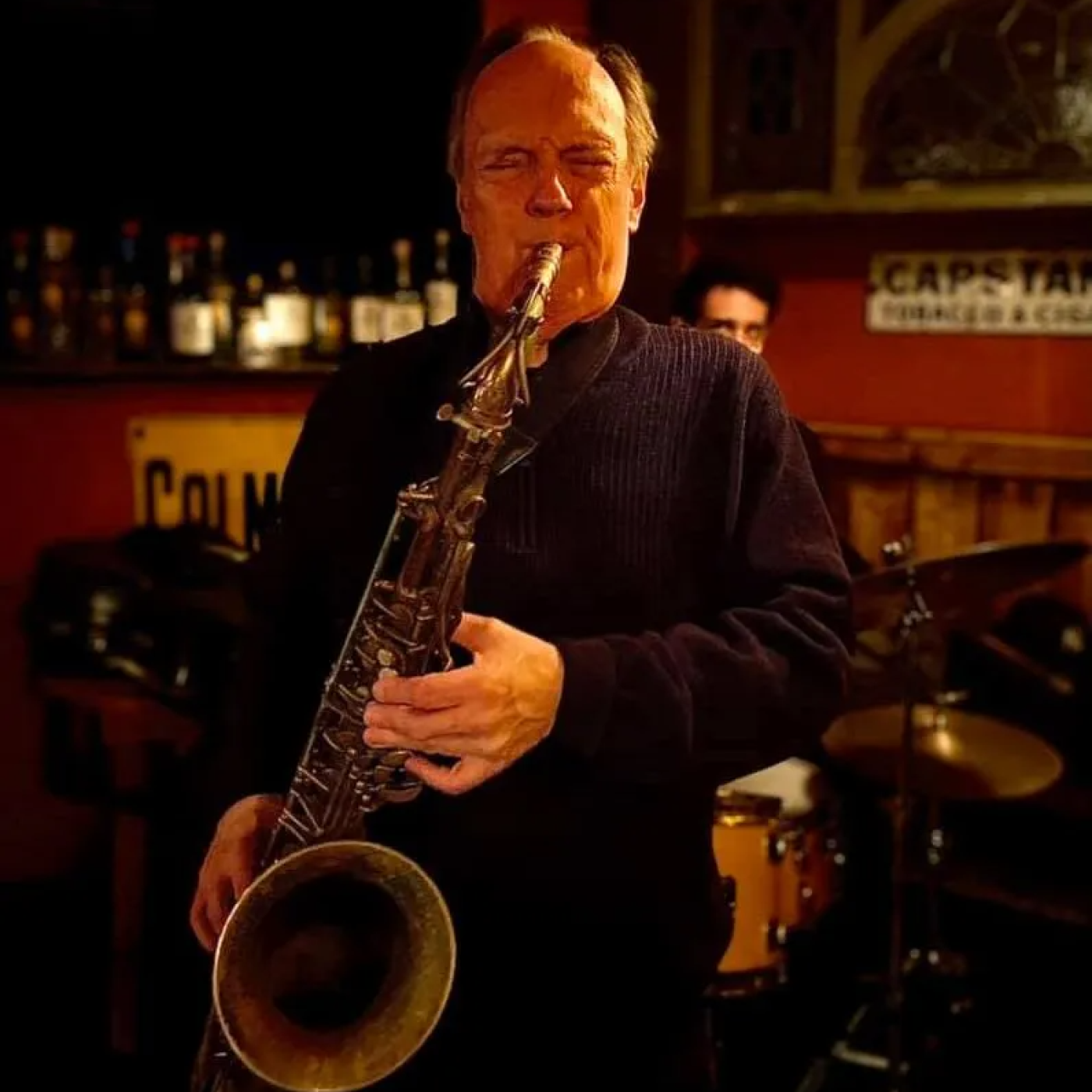 A man in a navy sweater playing a barry saxophone in a cafe