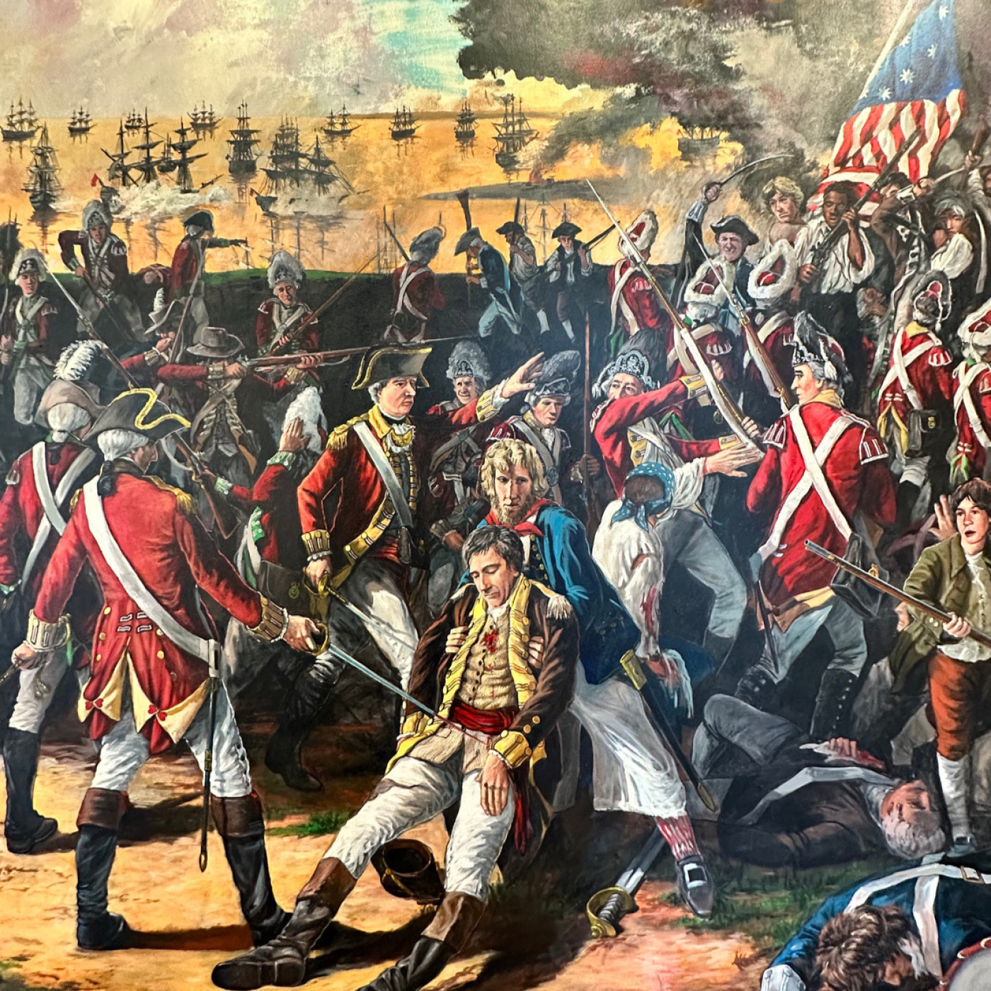 Painting of a Revolutionary War battle showing British and American forces fighting along the waterfront as a wounded officer is carried from the battlefield.