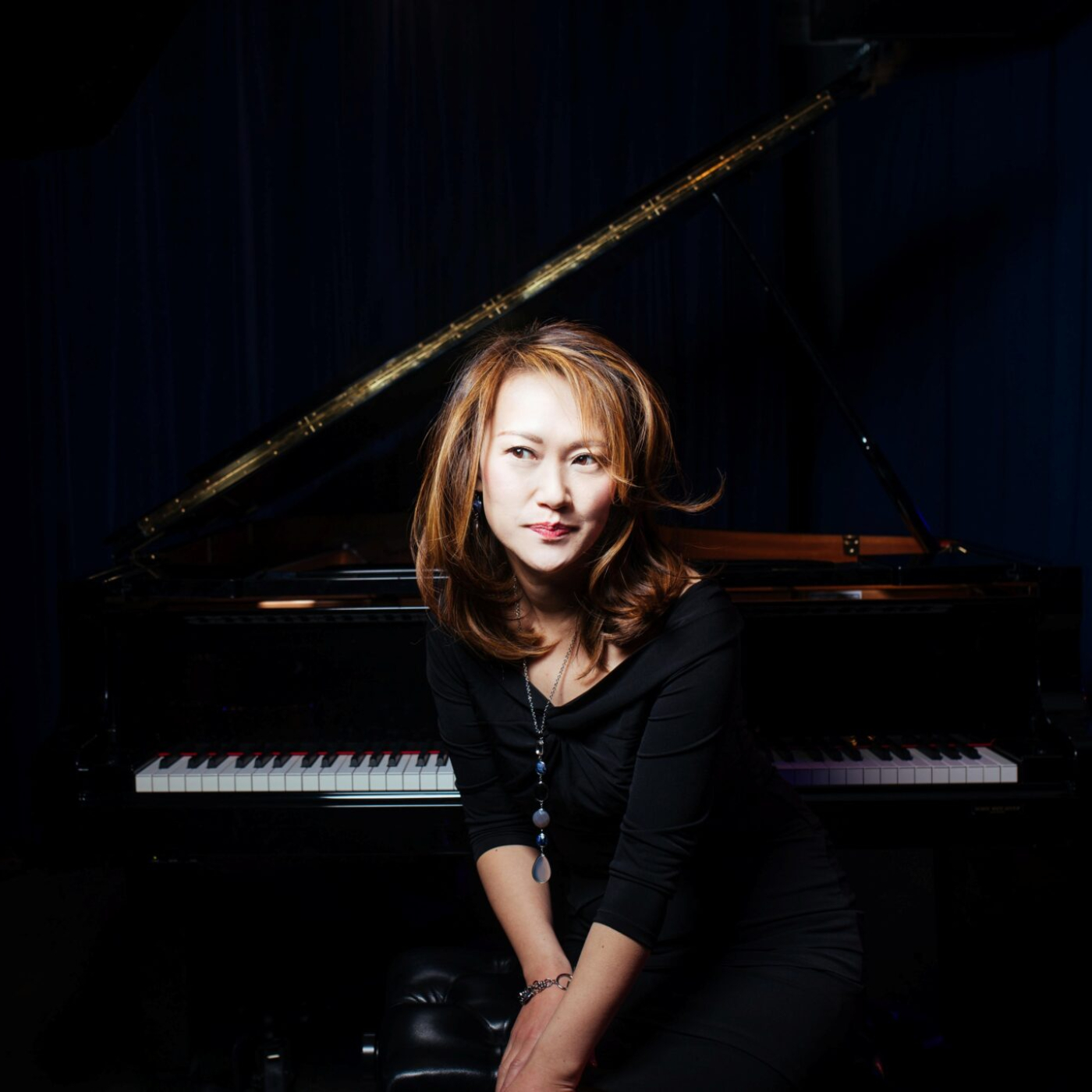 A woman in a black dress smiling in front of a grand piano