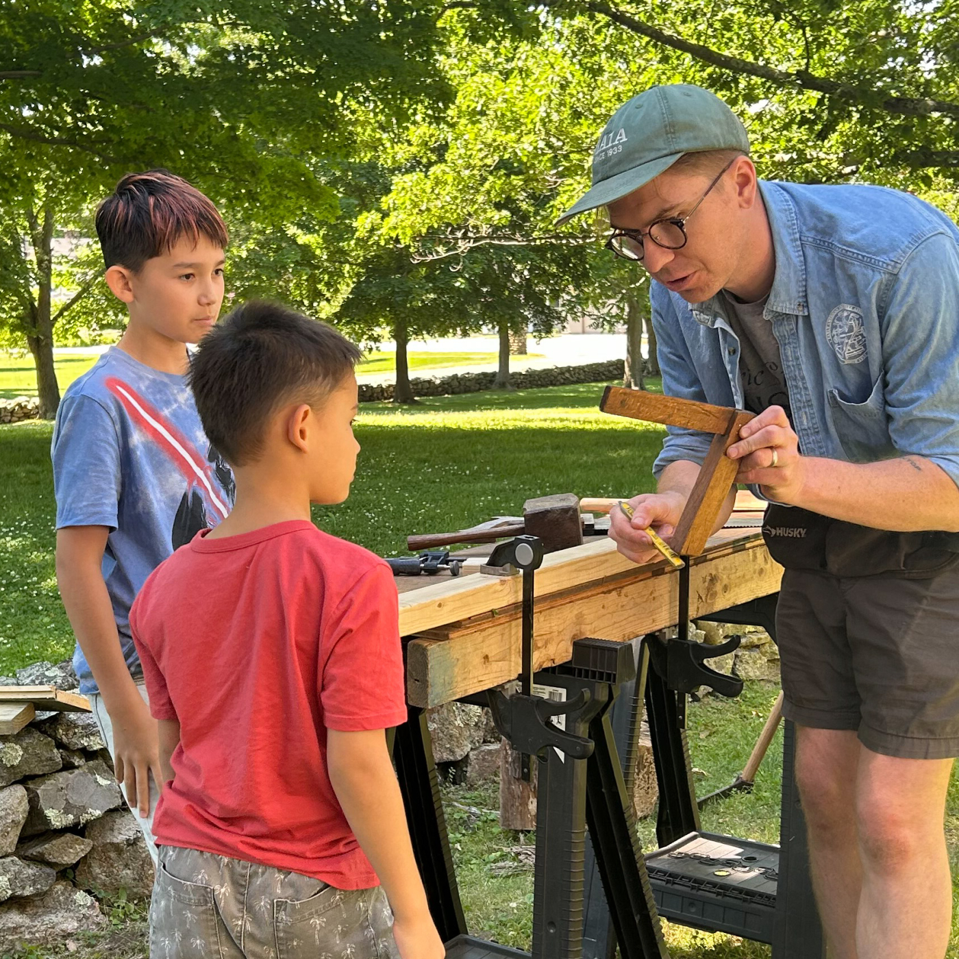 Two children watch as Andrew Rowand from the Eric Sloane Museum explains how to use a tool called a square