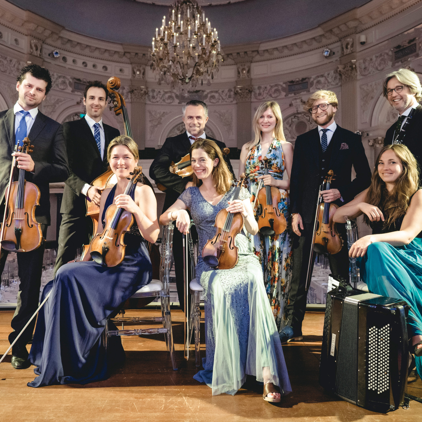 Group portrait of a chamber orchestra standing and seated in an ornate concert hall