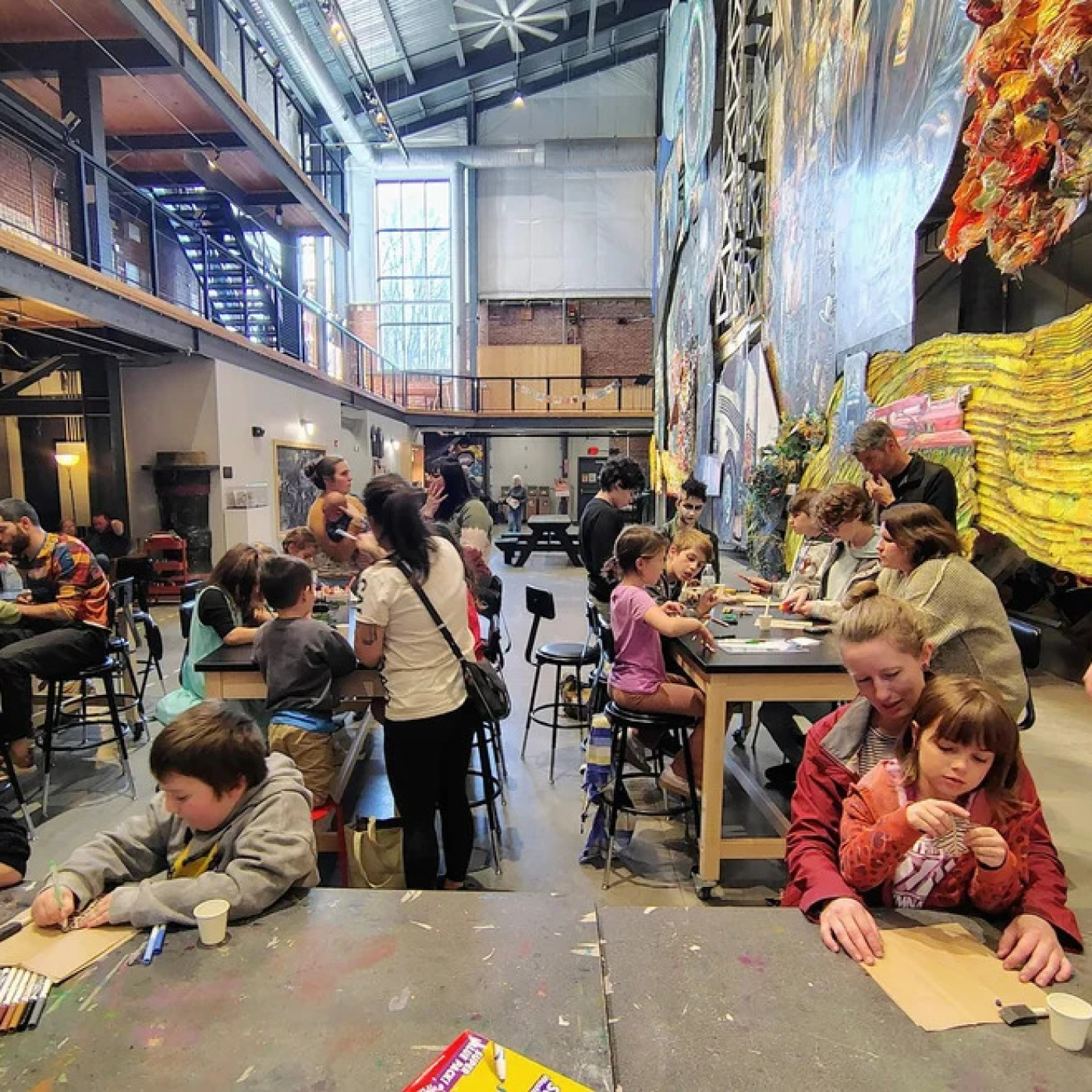 A crowd of various families doing arts and crafts together in a large open space.