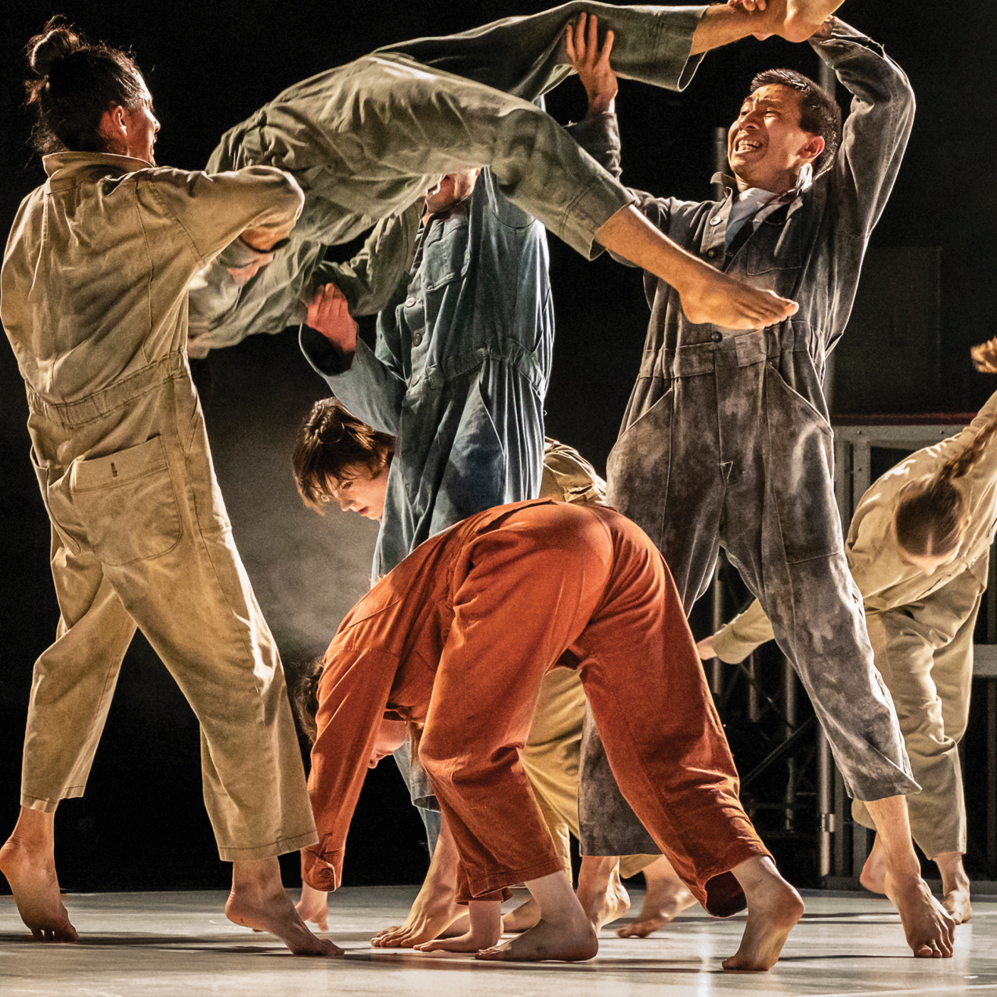 A group of dancers in coveralls perform dynamic movements