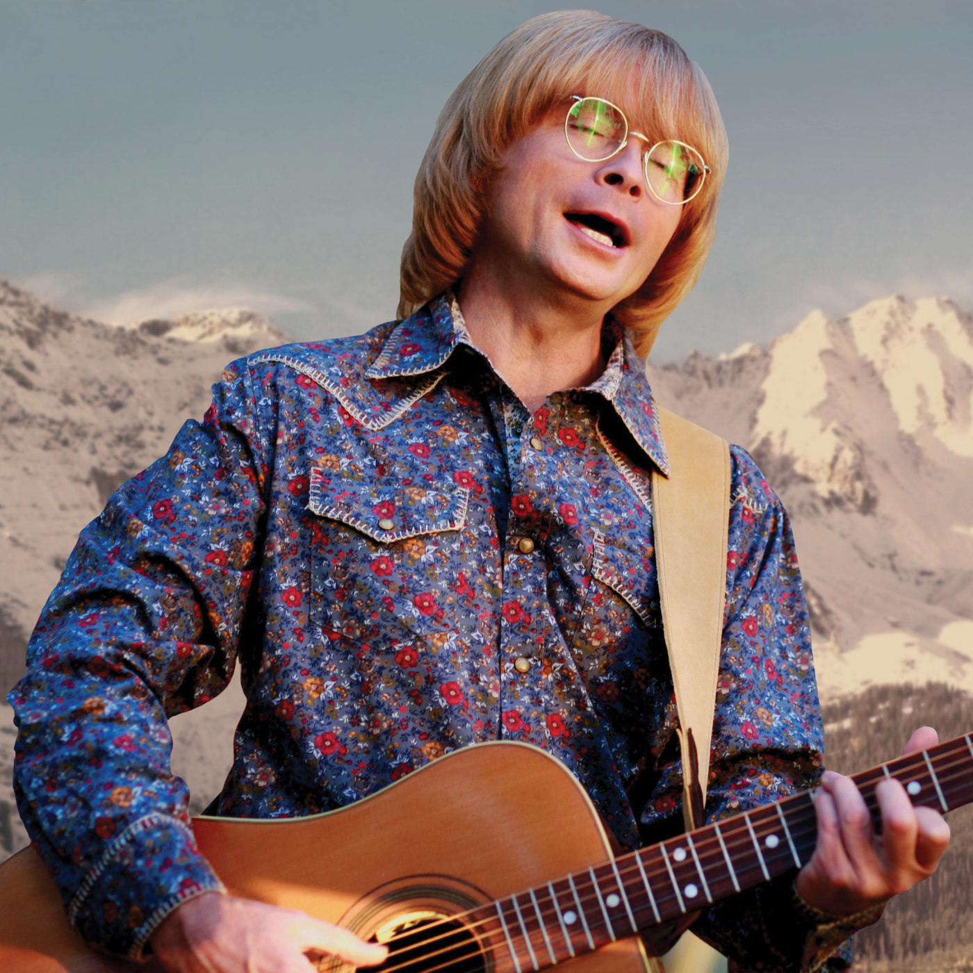 Man in floral shirt playing guitar with Rocky Mountain background 