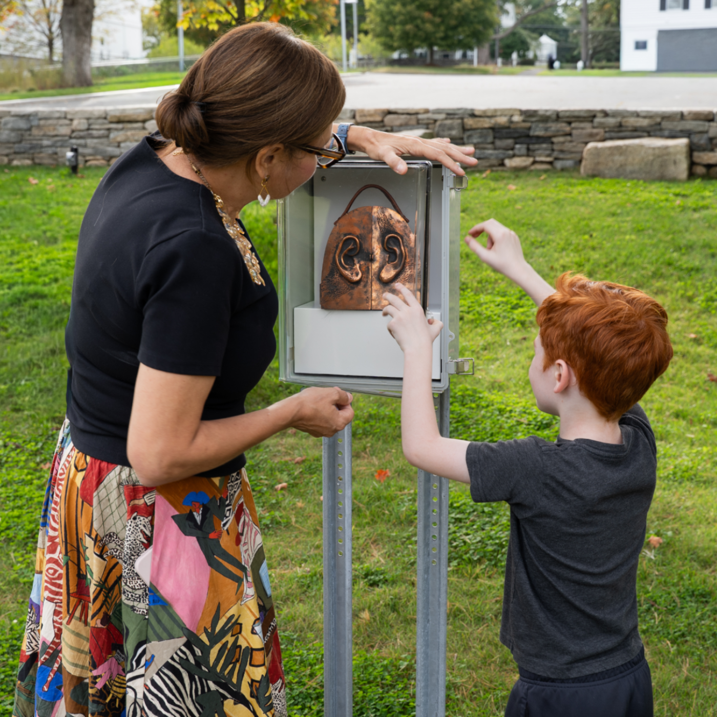 A woman and young boy opening a box with an artwork outside in the Museum's Sculpture Garden