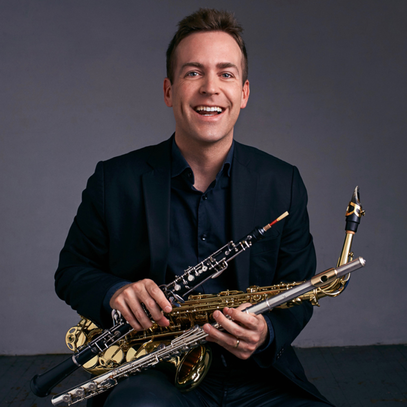Man in a suit smiling and holding a saxophone, flute, and oboe