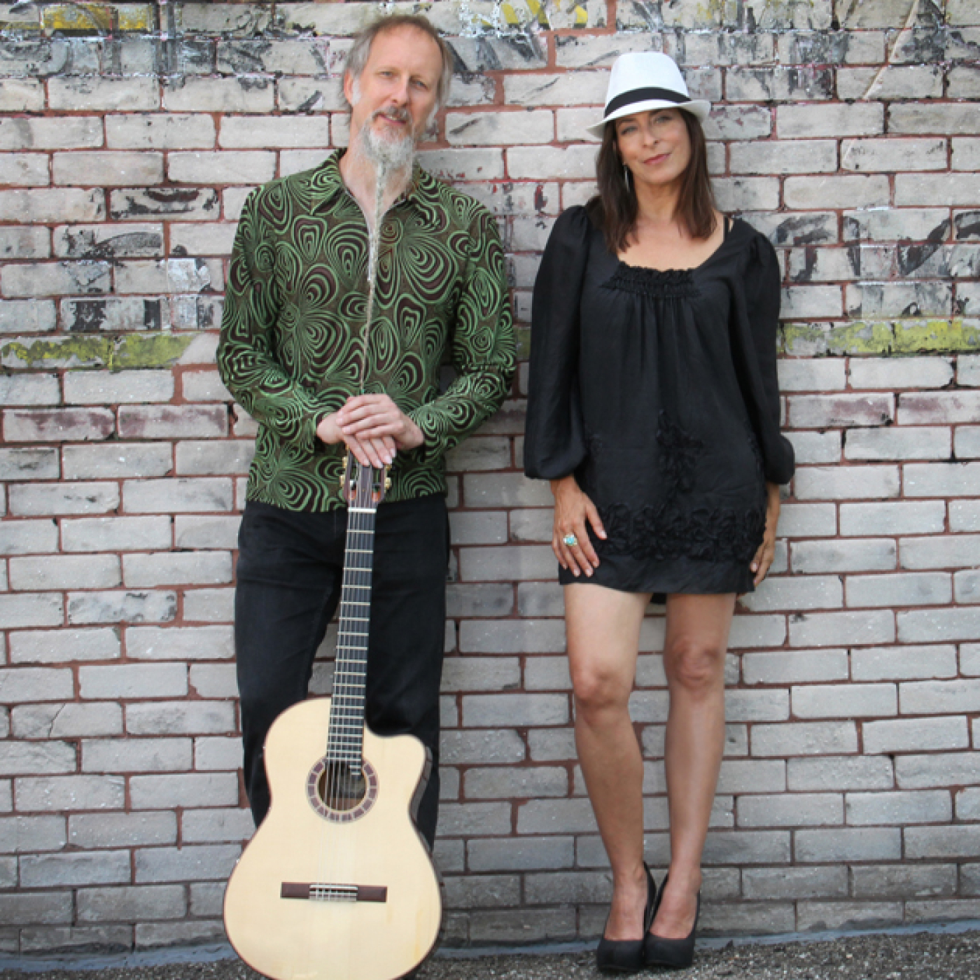 Man and woman leaning on brick wall with a guitar 