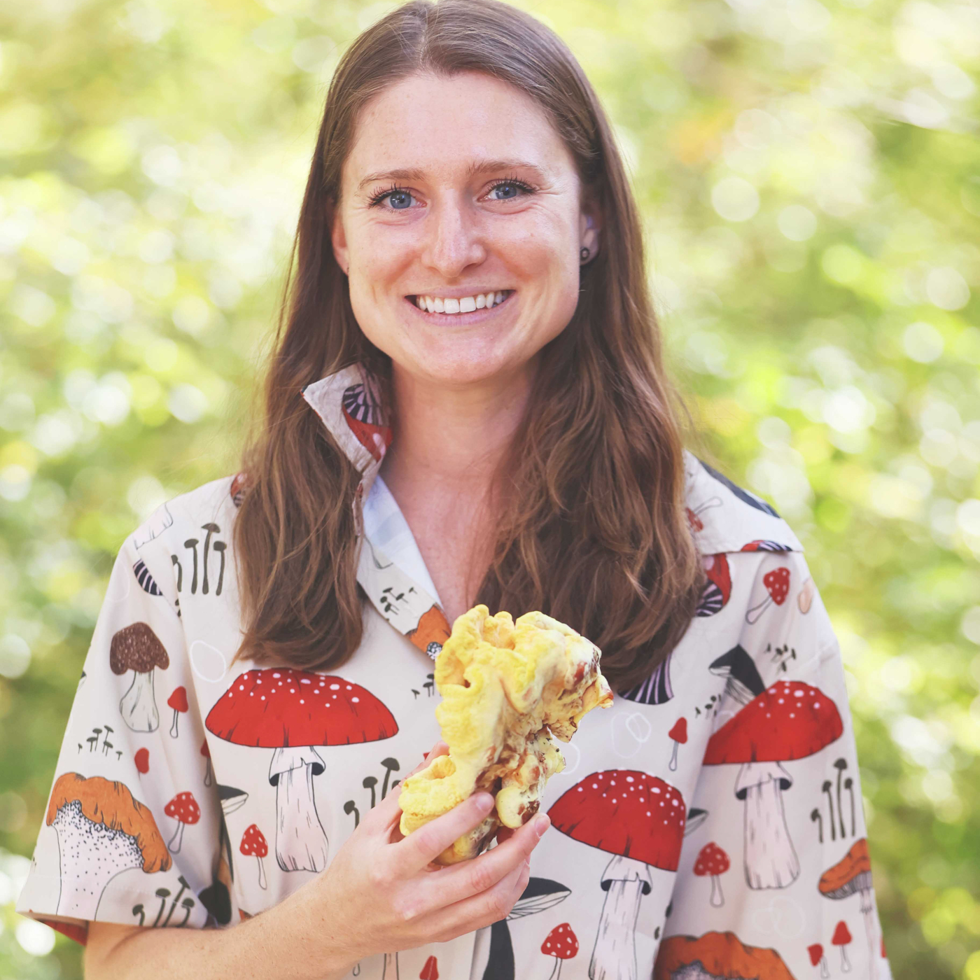 Woman holding a mushroom and wearing a shirt covered in mushroom illustrations