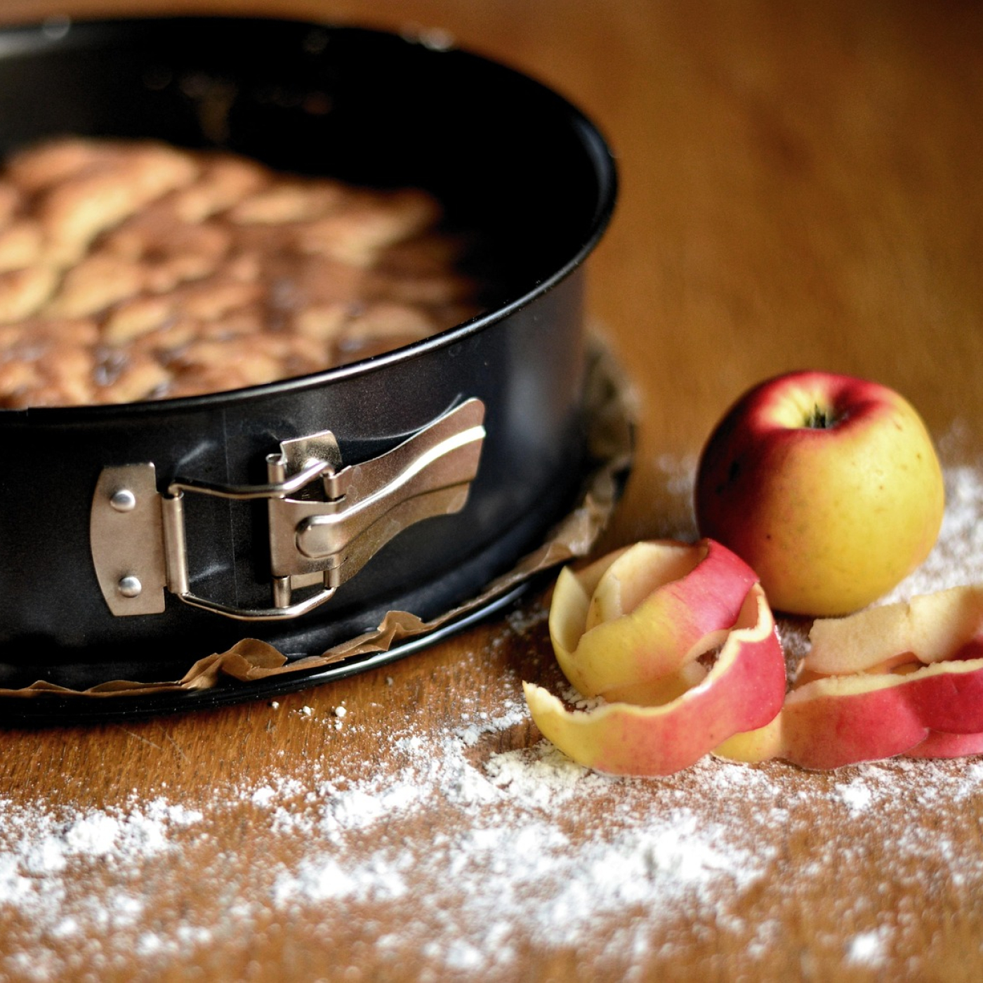 A peeled apple beside an apple cake in a springform pan