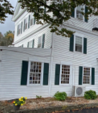Large white colonial building with green shutters and small garden