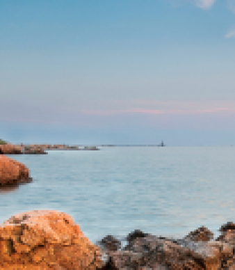 Lighthouse on rocky coast with sailboat on calm sea at sunset