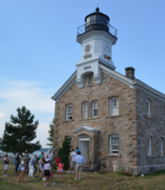 Stone lighthouse with people gathered outside near waterfront