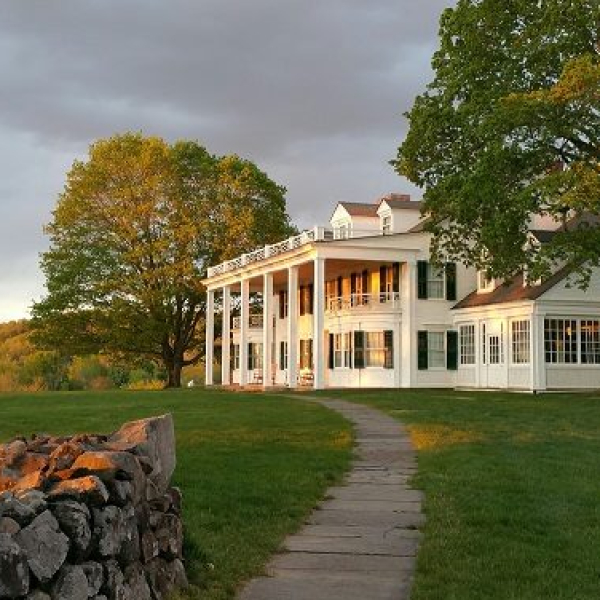 Historic white mansion with columns at sunset near stone wall and large trees