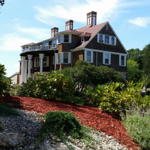 Historic house amidst landscaped garden with shrubs and flags in background