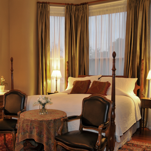 Elegant bedroom with four-poster bed, vintage chairs, and warm lighting