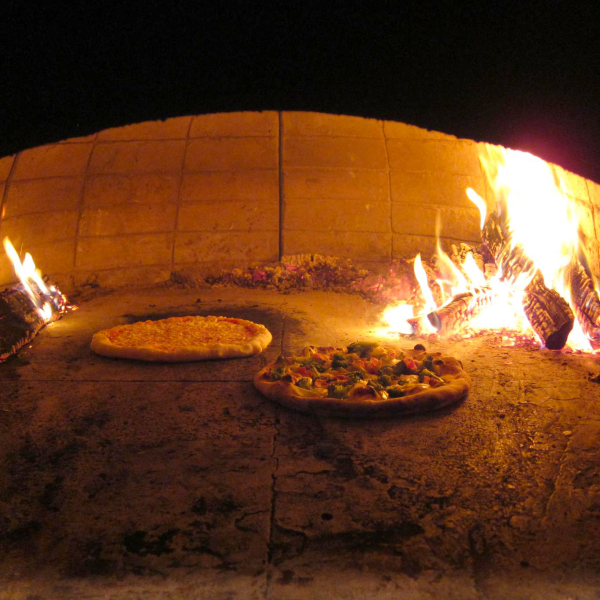 Two pizzas baking inside a traditional wood-fired brick oven