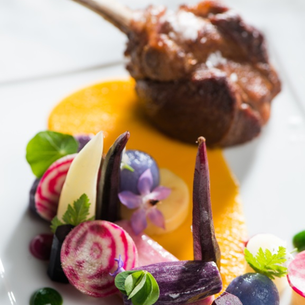 Roasted lamb chop with colorful seasonal vegetable garnish and sauce