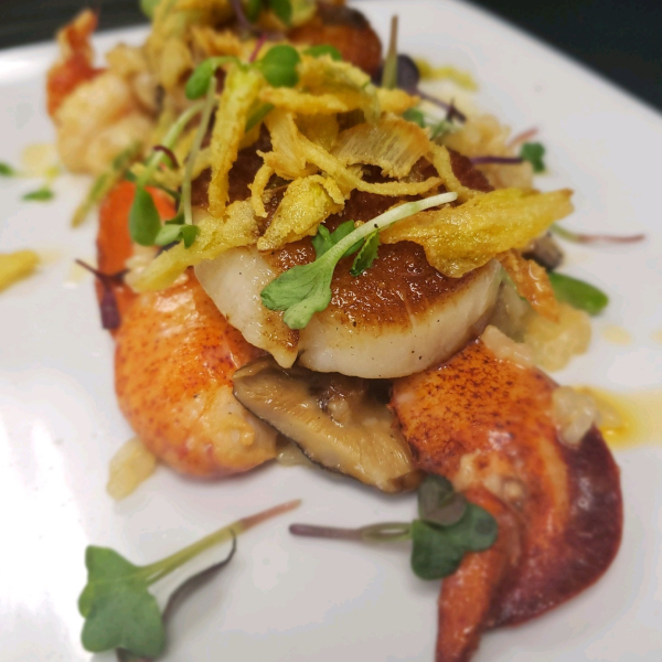 Seared scallops garnished with microgreens, fried onions, and lobster on white plate