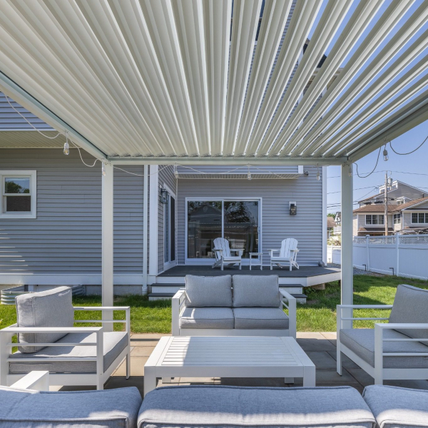 Outdoor lounge beneath an adjustable louvered pergola with shaded seating and lawn.