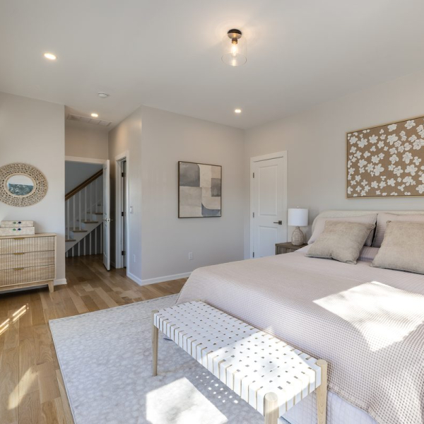 Light-filled king suite with wide-plank hardwood floors, upholstered bed, seating bench, and refined coastal decor. 