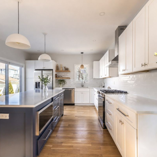 Chef’s kitchen with a navy island, quartz countertops, pendant lighting, stainless appliances, and wide-plank hardwood floors