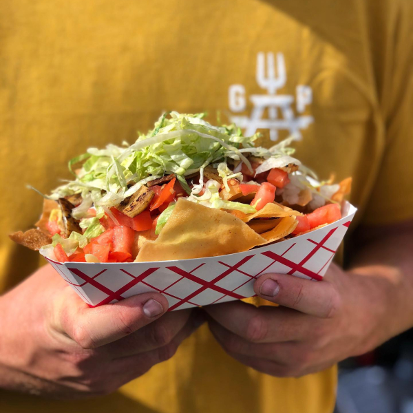 Person holding nachos topped with lettuce, tomatoes, and grilled meat