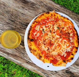 Tomato and cheese pizza on paper plate with drink on wooden table