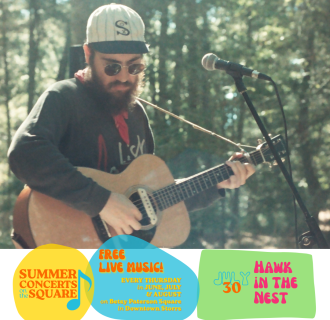A bearded man stands in the woods, playing a guitar; he wears a retro White Sox baseball cap and round sunglasses