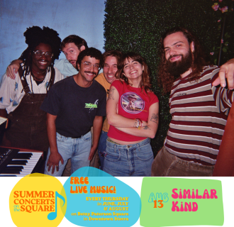 Six young people smile and pose for the camera in front of a wall covered in leaves