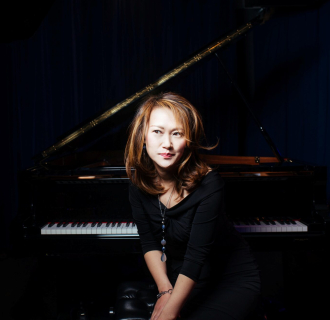 A woman in a black dress smiling in front of a grand piano