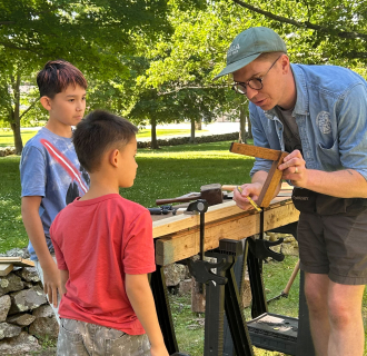 Two children watch as Andrew Rowand from the Eric Sloane Museum explains how to use a tool called a square