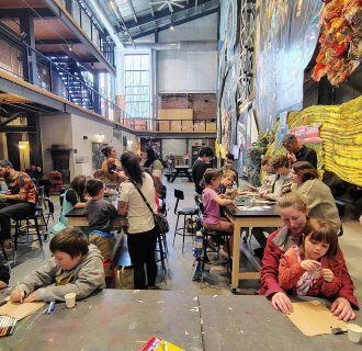 A crowd of various families doing arts and crafts together in a large open space.